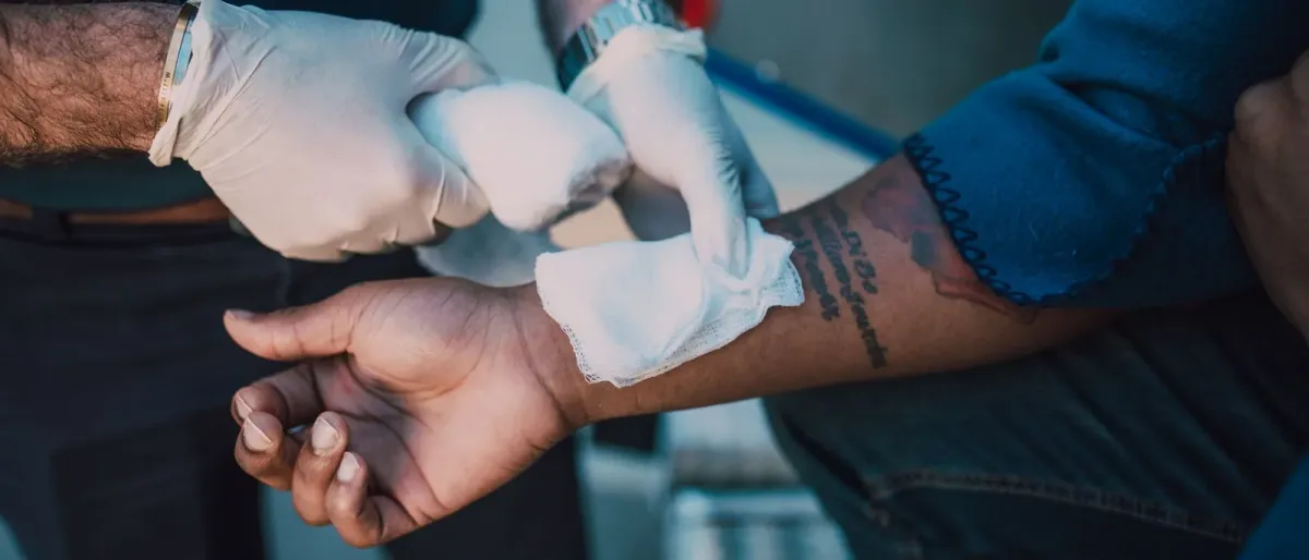 Gloved hands pressing a gauze dressing onto a person's forearm