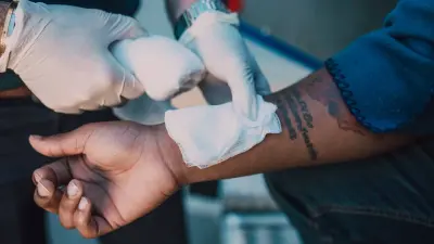 Gloved hands pressing a gauze dressing onto a person's forearm