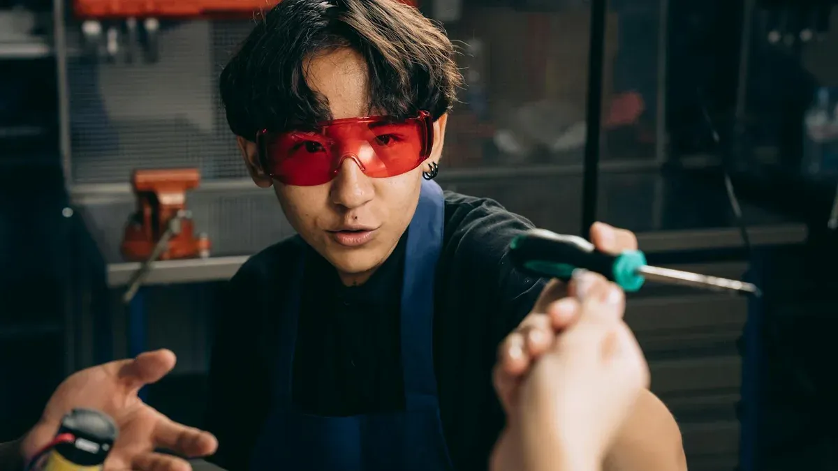 Two students in safety glasses working at a school carpentry bench with framing lumber and a measuring square